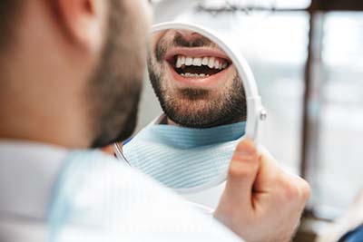 Man looking at teeth in small mirror after dental fillings columbia md