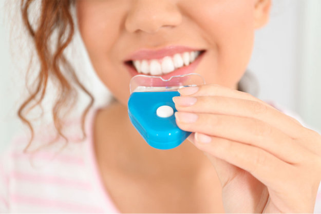 Whitening woman uses a tooth whitener at home