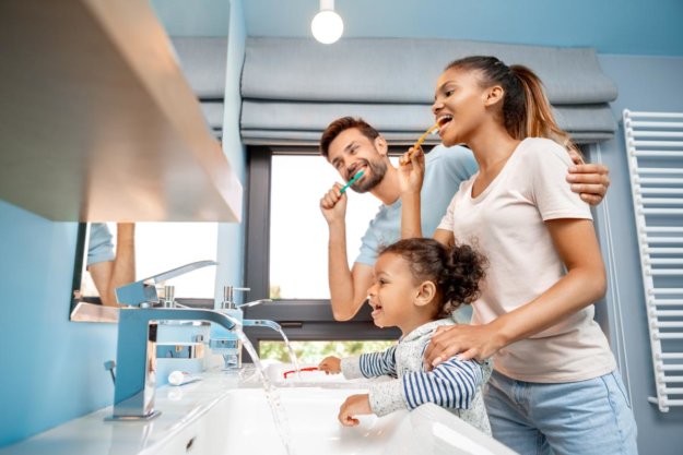 Dental Care Tips for Parents of Young Children parents helping their daughter with child dental care by brushing their teeth together