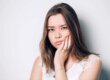 woman holding the side of her jaw wonders about the most common wisdom teeth removal age