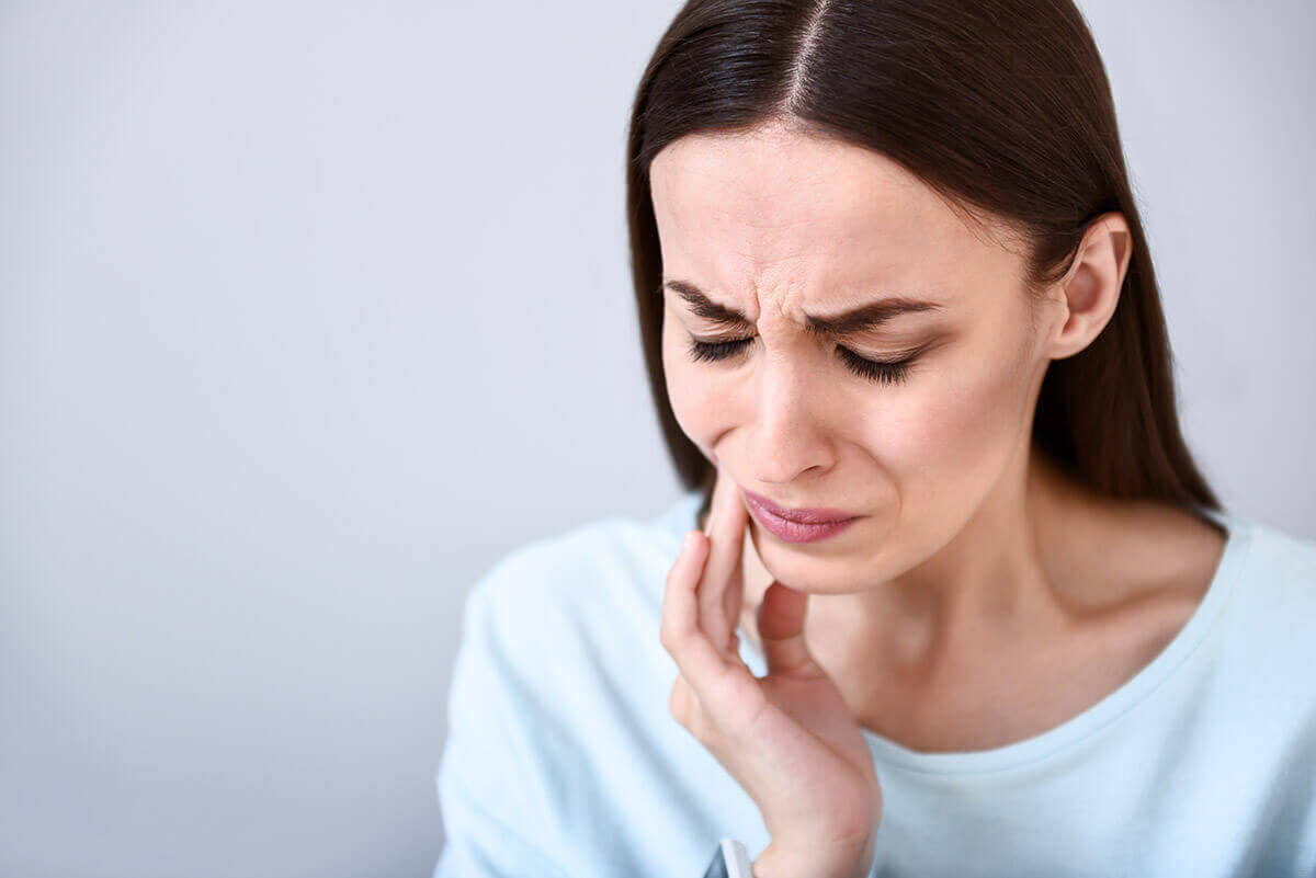 Does Nerve Pain in Tooth Go Away_ woman touches side of face while experiencing nerve pain in tooth