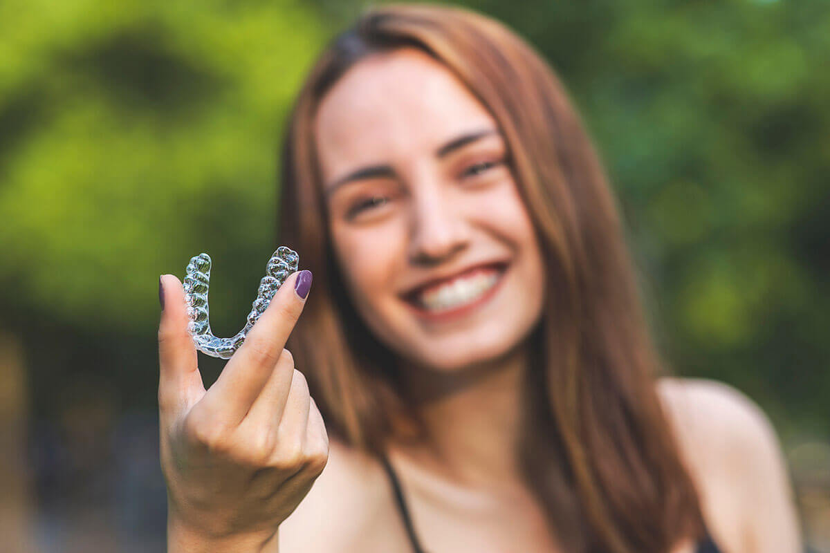 How Much Does Invisalign Cost Woman holding up an appliance wondering, "How much does Invisalign cost?"